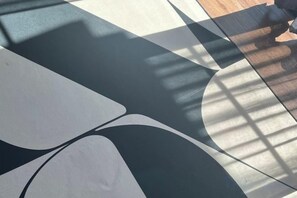 A floor with a geometric pattern, possibly a rug or mat, and a shadow cast by a window or light source.