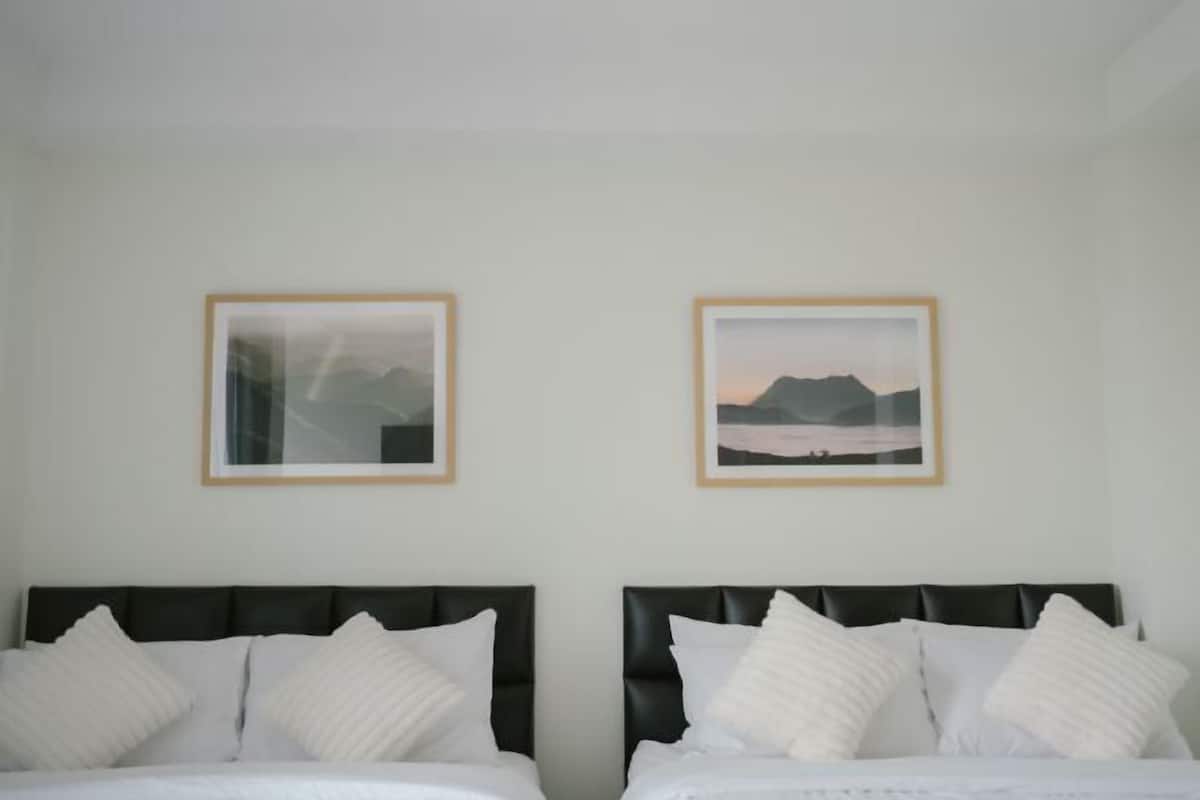 Ein Hotelzimmer mit zwei Betten, jeweils mit schwarzem Kopfteil und weißer Bettwäsche. An der Wand hängen zwei gerahmte Bilder.