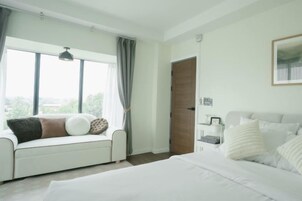 Un dormitorio con cama, sofá, mesita de noche, ventana y puerta.