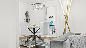 Un comedor moderno con una mesa y sillas blancas, una lámpara colgante y vista a la cocina.