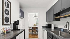 A modern kitchen with dark cabinetry, a built-in dishwasher, and a dining area with a table and chairs. - Exclusive Louisville king suite near bourbon trail (Louisville)