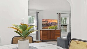 A dining area with a marble table, a potted plant, and a television displaying a cityscape. - Exclusive Louisville king suite near bourbon trail (Louisville)