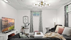 Ein modernes Wohnzimmer mit großem Flachbildfernseher, einer Couch, einem Couchtisch und einer Deckenleuchte.