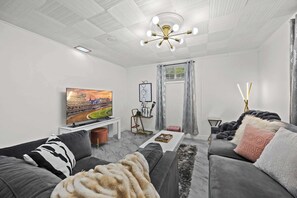 Una sala de estar moderna con televisor, sofás grises, una mesa de centro y una lámpara del techo.