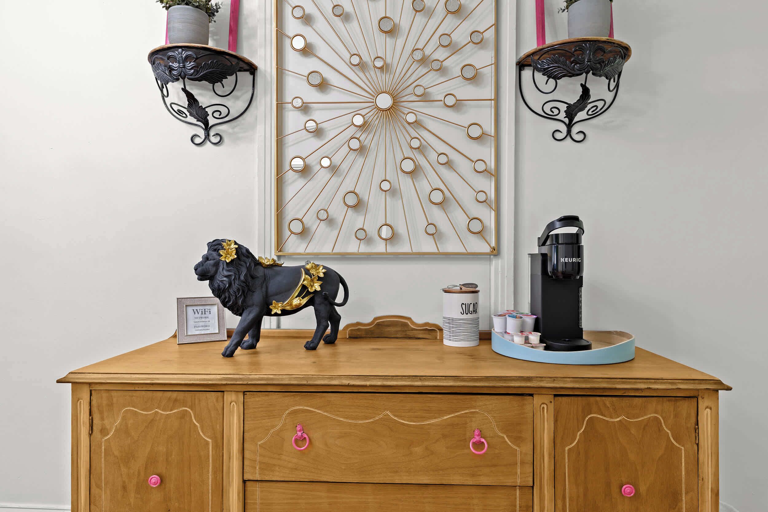 A wooden dresser with a decorative lion figurine, a coffee machine, and a wall-mounted circular light fixture.