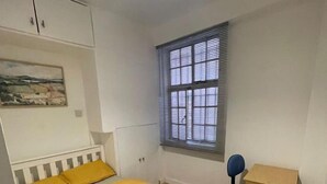 Ein Schlafzimmer mit Bett, Fenster, Stuhl und kleinem Schreibtisch.