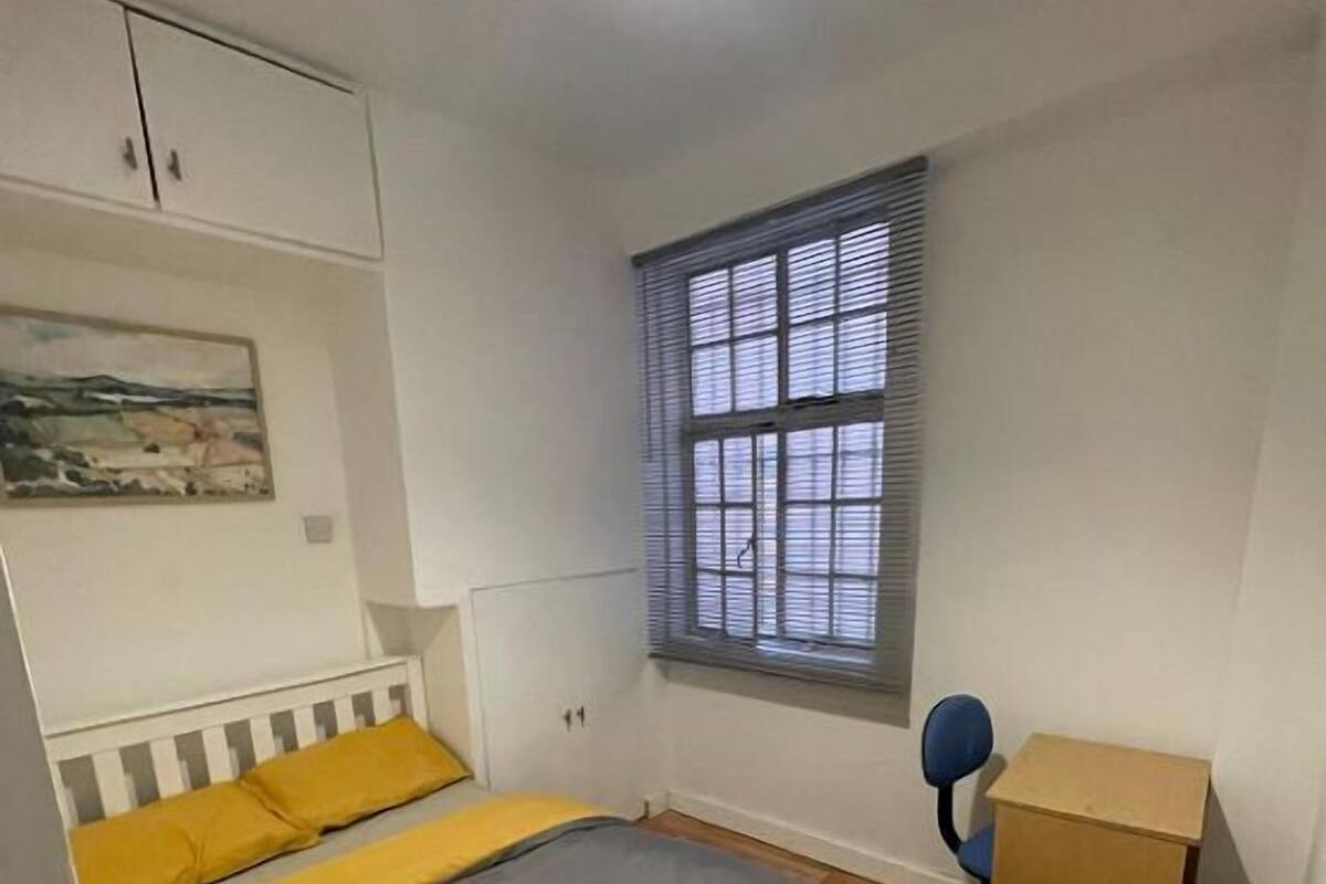 A bedroom with a bed, a window, a chair, and a small desk.