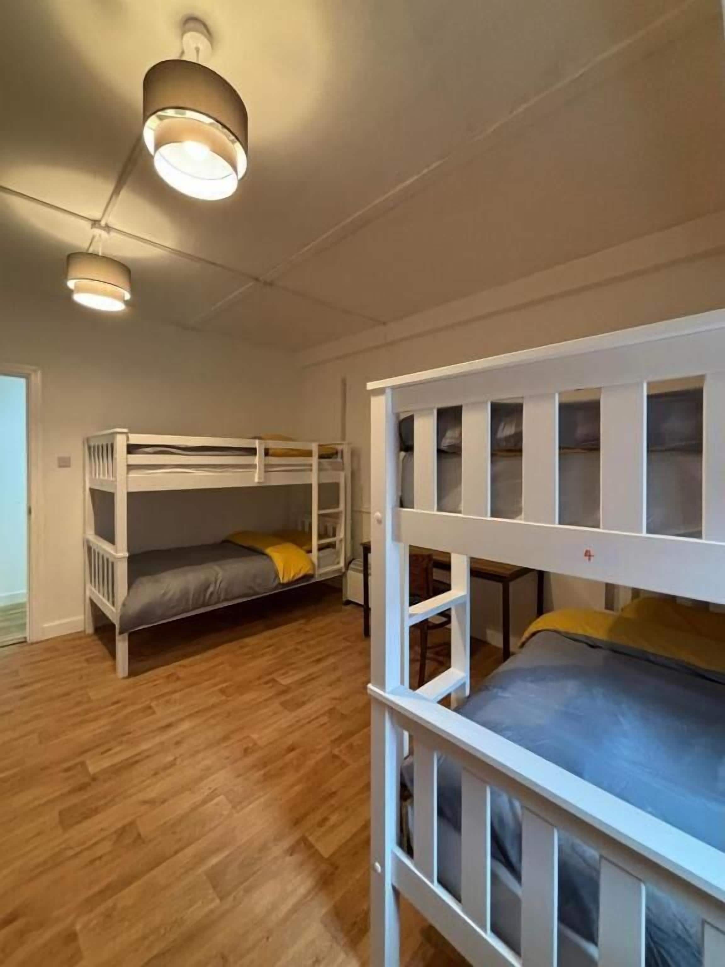 A room with two bunk beds, wooden flooring, and a ceiling light fixture.