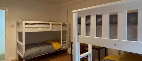 A room with two bunk beds, wooden flooring, and a ceiling light fixture.
