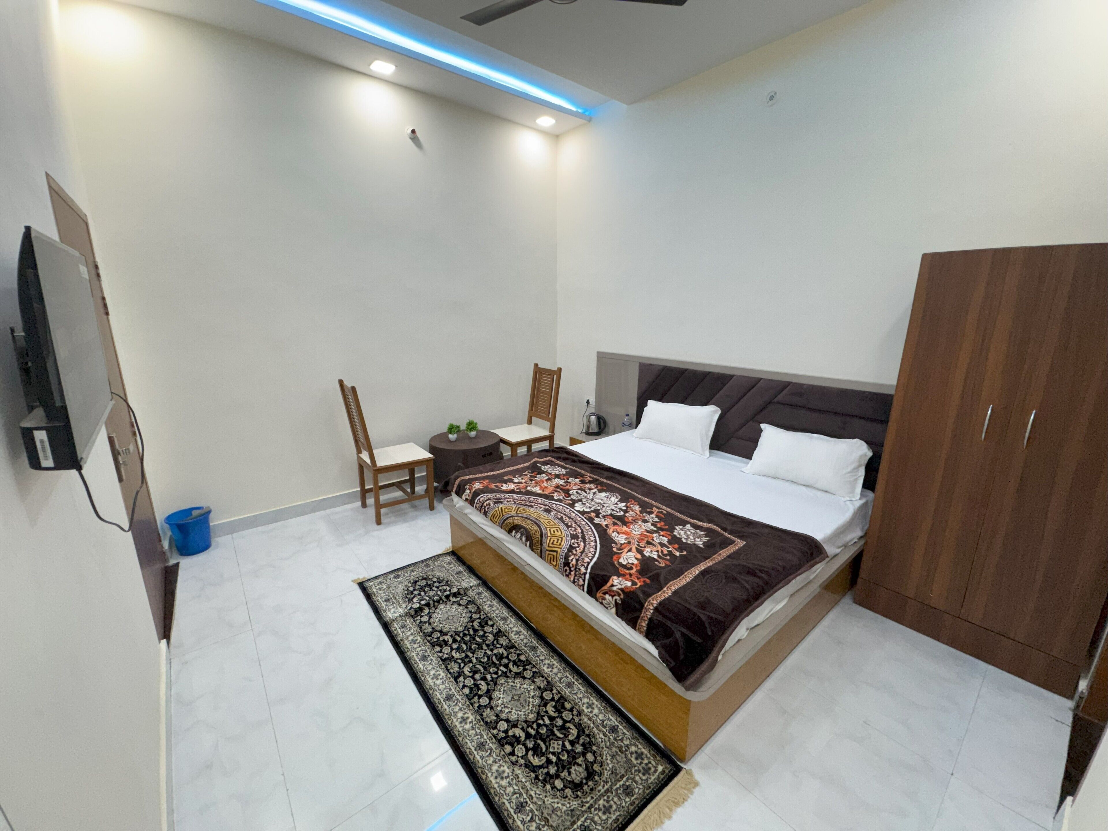 A bedroom with a bed, two chairs, a small table, a wardrobe, and a TV.