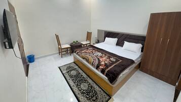 A bedroom with a bed, two chairs, a small table, a wardrobe, and a TV.