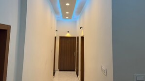 A narrow hallway with a wooden door at the end, recessed lighting, and a light strip along the ceiling. - It's Braj Raj Home Stay  (Mathura)