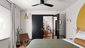 Une chambre moderne avec un lit, un ventilateur de plafond, une porte donnant sur un espace de vie et une plante en pot.