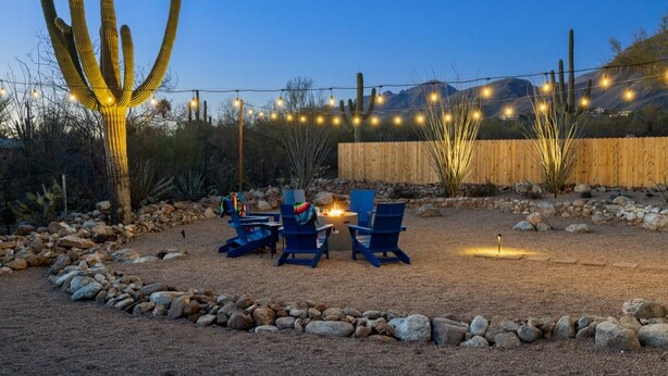 Un paysage désertique avec un cactus, une clôture en bois et un foyer avec des chaises.