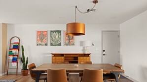 Un coin repas avec une table en bois, quatre chaises, un luminaire suspendu en cuivre et des œuvres d’art murales.