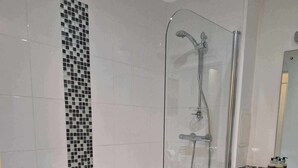 Un baño moderno con ducha de vidrio, una bañera blanca y un lavamanos con artículos de aseo.