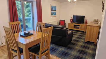 Ein gemütliches Wohnzimmer mit Holzesstisch, schwarzem Ledersofa und Fernseher.
