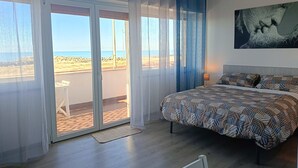 Un dormitorio con cama, mesita de noche, un cuadro y vistas a la playa a través de una puerta corrediza.