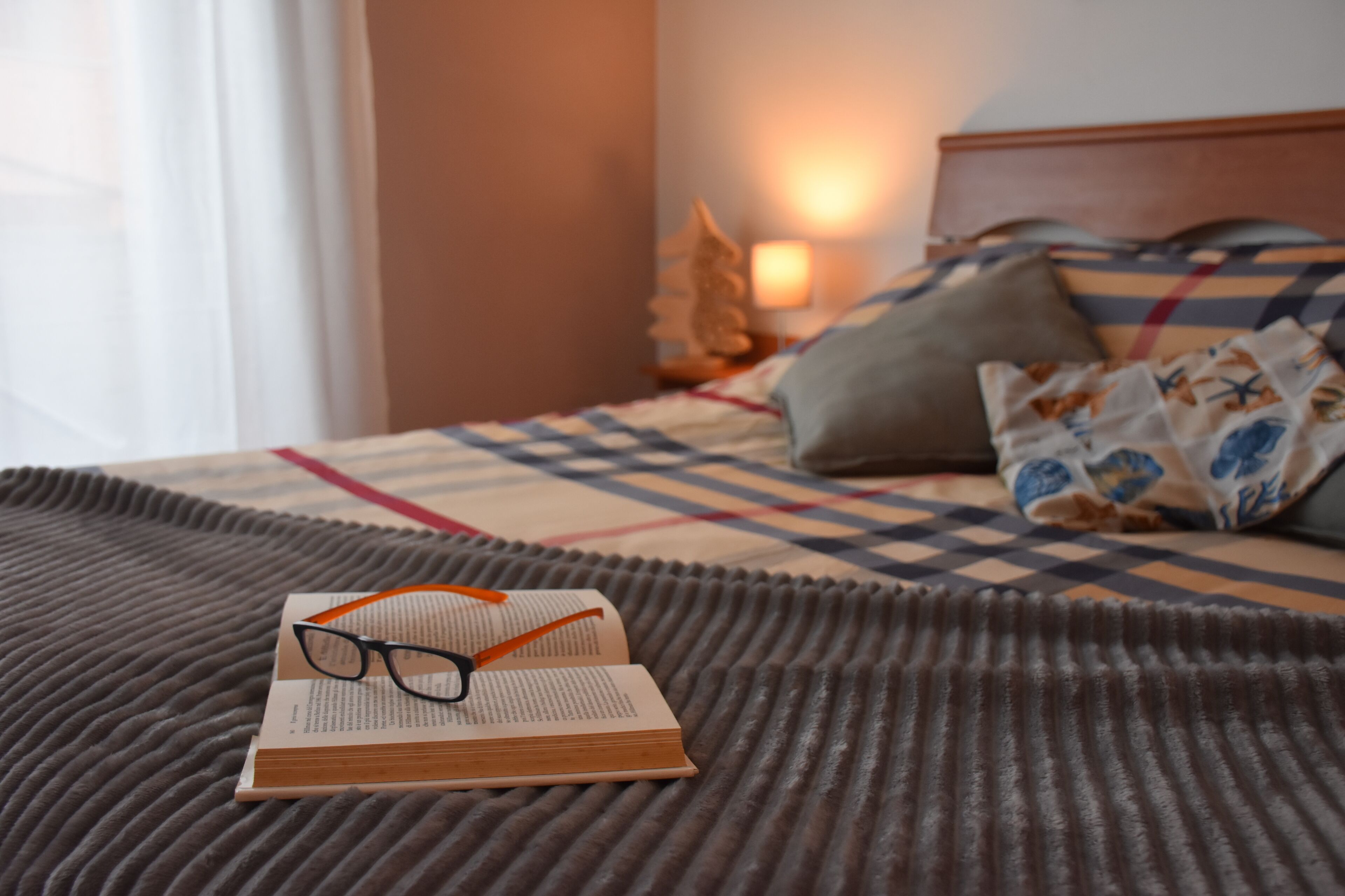 A bed with a checkered bedspread, a book, and glasses on a textured blanket.