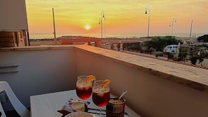 Un balcón con una mesa dispuesta para dos personas, que incluye una bandeja con dos bebidas, un bol de papas fritas y una lata de chips.