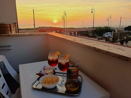 En balkon med et bord dækket til to personer, med en bakke, der indeholder to drikkevarer, en skål med pommes frites og en dåse chips.