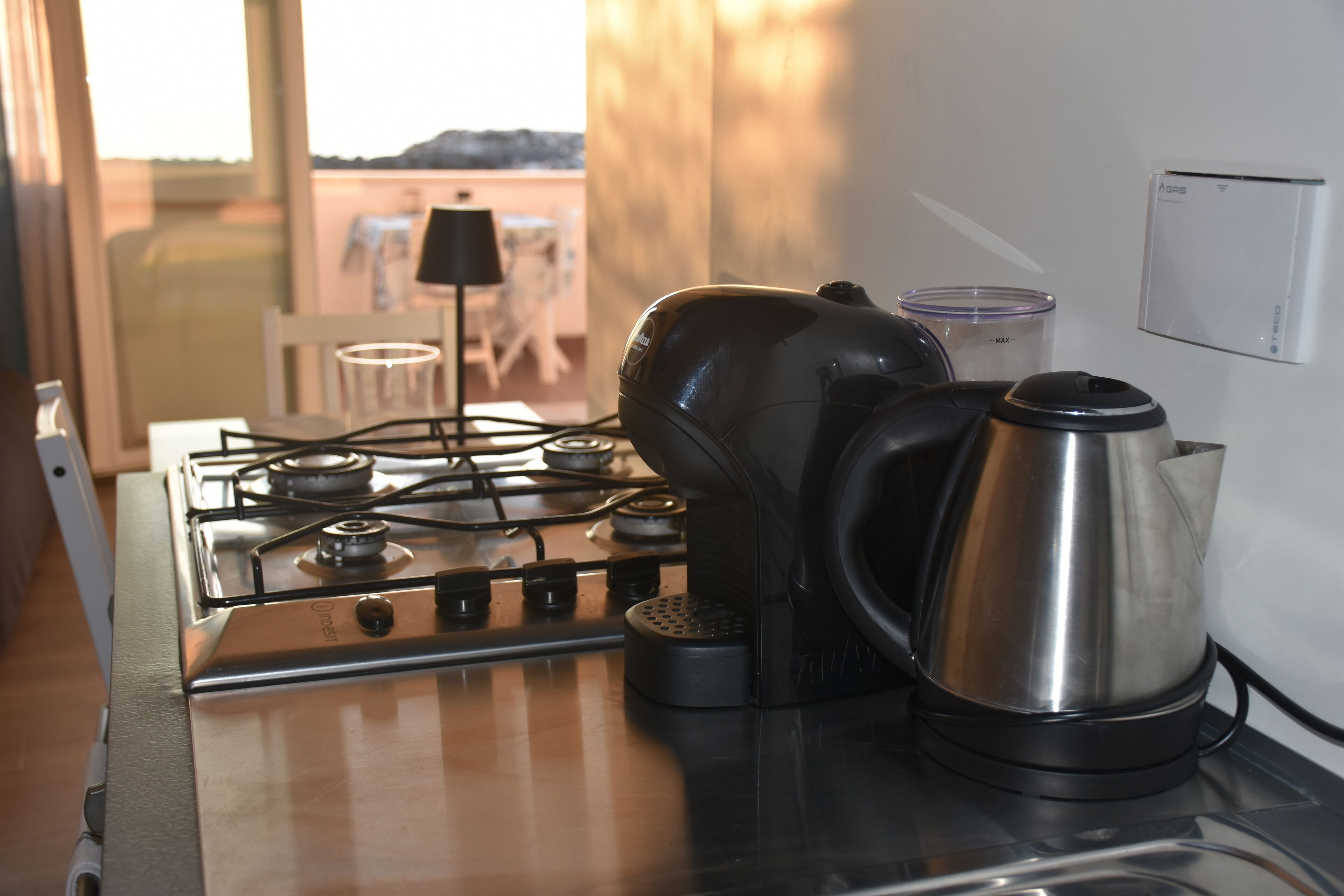 A kitchen with a gas stove, a kettle, and a coffee maker.