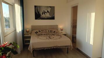 Een slaapkamer met een bed, twee bedlampjes, een kunstwerk aan de muur en een plant in een pot.
