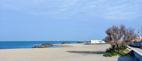 A beach with a clear sky, a sandy shore, and a few rocks.