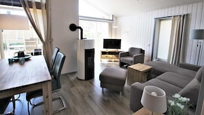 Ein modernes Wohnzimmer mit Esstisch aus Holz, grauem Sofa und Fernseher.