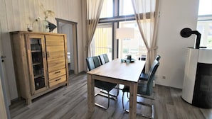 Ein Essbereich mit Holztisch und -stühlen, einem Schrank mit Glastüren und einem großen Fenster mit Vorhängen.
