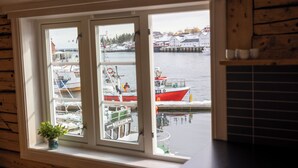 Vista desde una ventana con interior de madera, que da a un puerto con barcos y edificios.