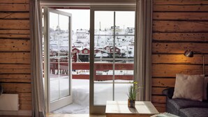 Una habitación acogedora con detalles de madera, un ventanal corredero que da a un espacio exterior nevado, una mesita con una planta y un sofá con una lámpara.