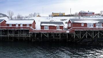 Un edificio frente al agua con fachada roja y detalles blancos, que cuenta con varias ventanas y un muelle que se adentra en el agua.