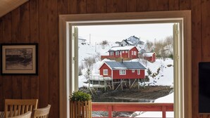 Un interior de madera con vista a una casa roja sobre pilotes a través de una puerta abierta.
