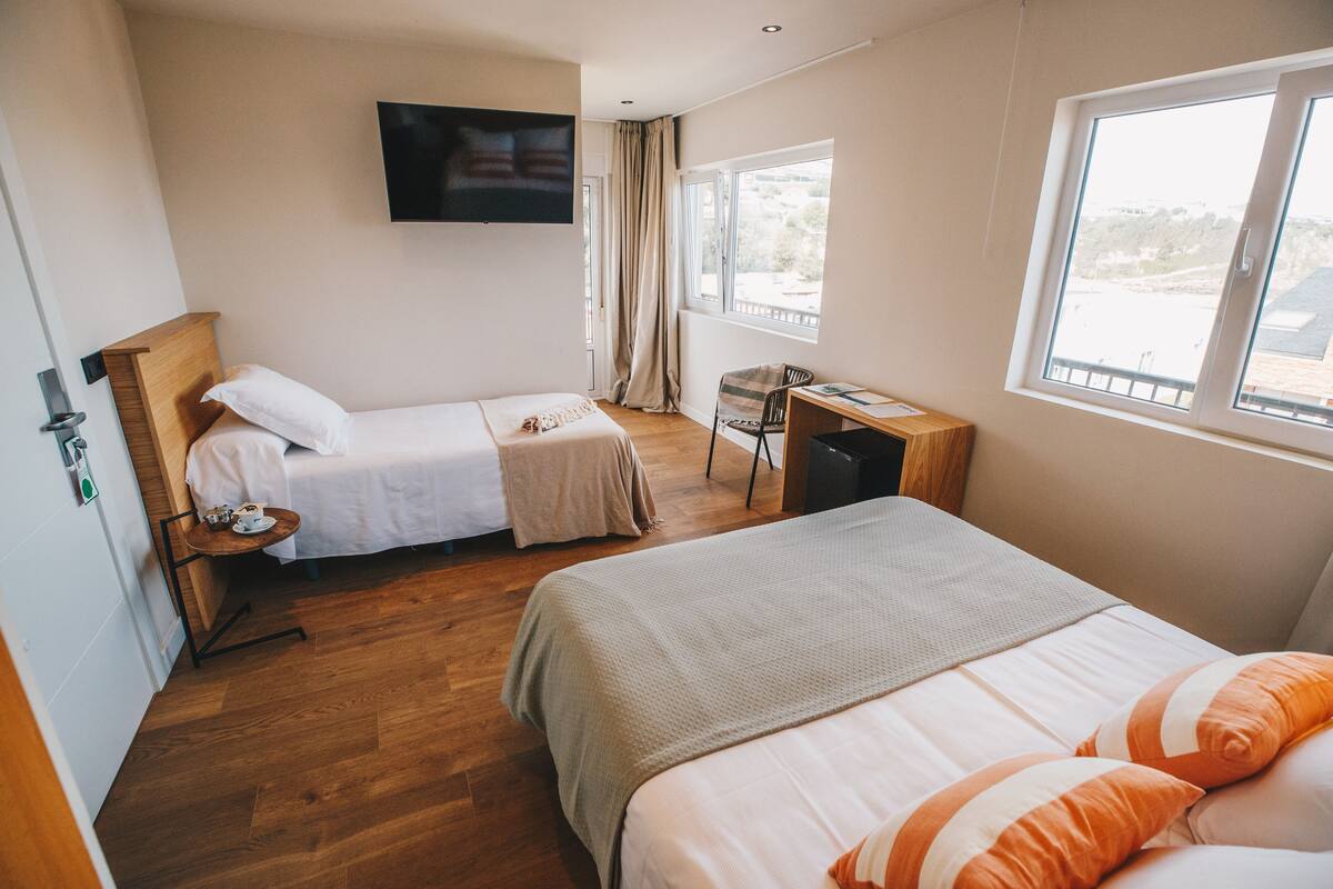 Une chambre d’hôtel avec deux lits, un bureau, une chaise, une télévision et une fenêtre donnant sur un beau paysage.