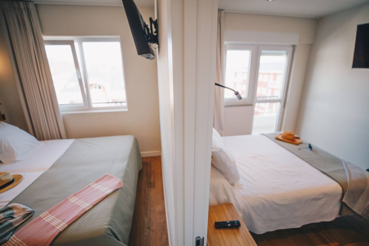Une chambre d’hôtel avec deux lits, une fenêtre, une télécommande sur la table de chevet et une porte.