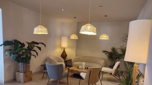 Una sala moderna con un sofá, dos sillones, una mesa de centro y lámparas colgantes. Hay plantas en macetas y una lámpara en una mesita auxiliar.