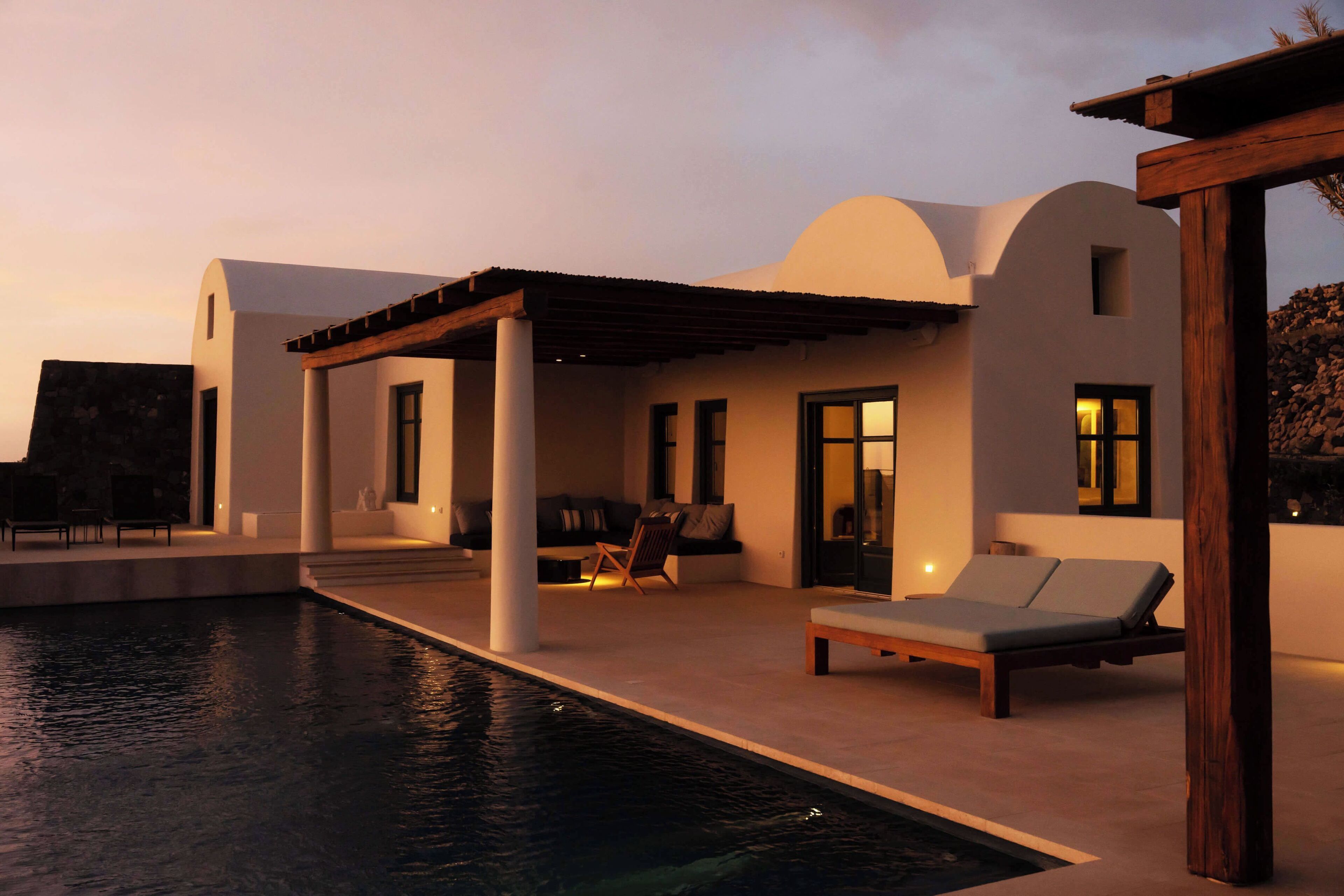 A modern poolside area with a lounge chair, a small table, and a covered seating area.