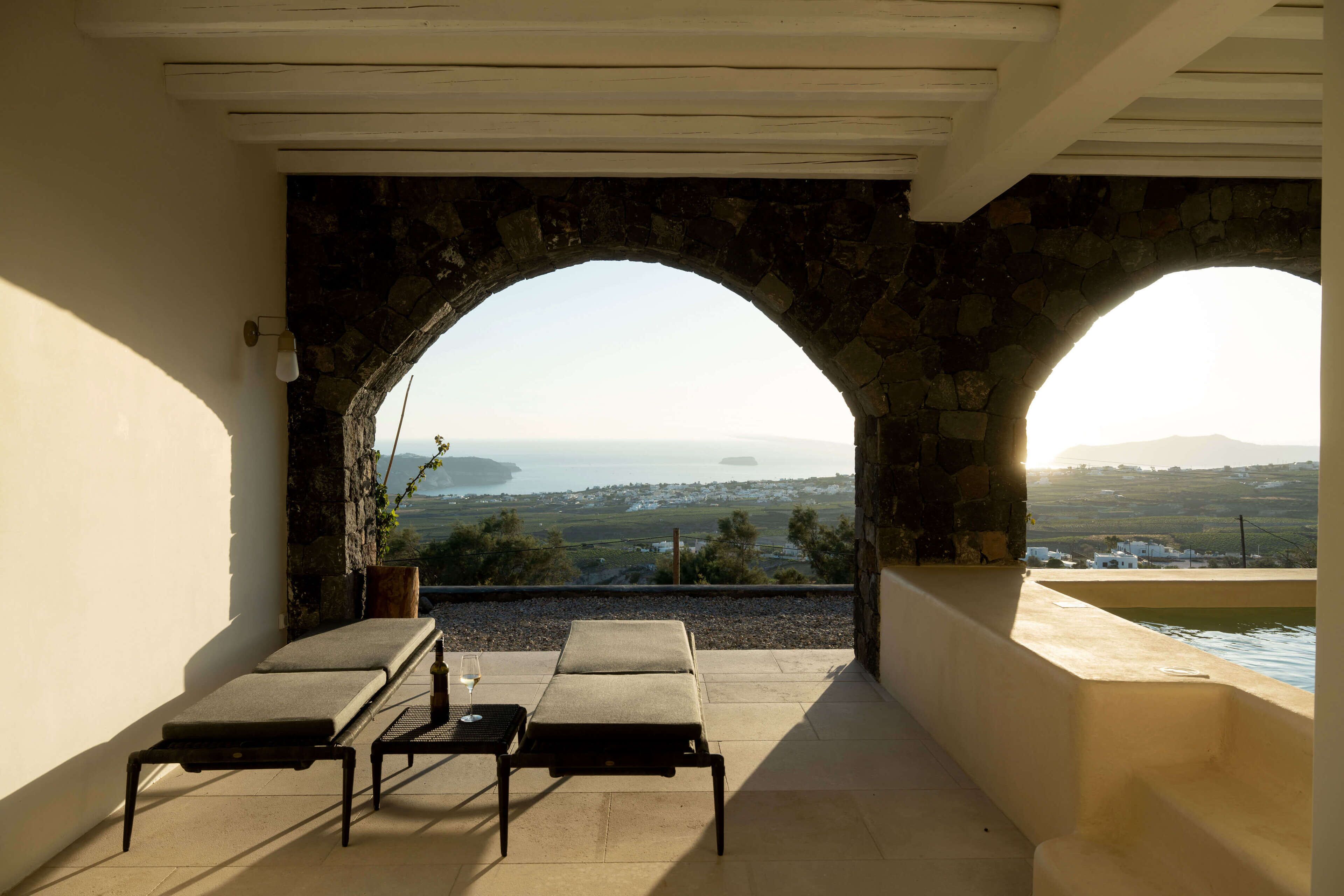 Eine Terrasse mit zwei Liegestühlen und einem Tisch, mit Blick auf eine reizvolle Landschaft, die durch eine Rundbogenkonstruktion aus Stein zu sehen ist.