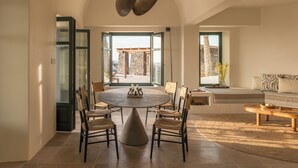 A dining area with a round table, six chairs, and a central light fixture. - Patina Vivera Estate (Santorini)