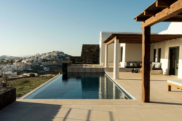 Zwembadgedeelte met uitzicht op een heuvelstad, een houten pergola en een moderne buitenlounge.
