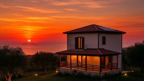 A two-story house with a balcony, a view of the sunset over the sea, and a mountain in the background. - Kitty House (Spilinga)