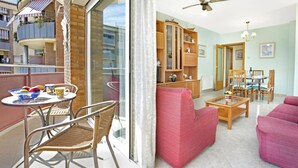 Un balcón con sillas de mimbre y una mesa, una sala de estar con un sofá y una mesita de centro, y un mueble de madera con puertas de cristal.