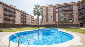 Una piscina rodeada de edificios de apartamentos con balcones, una palmera y un área verde.