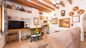 A cozy living room with a sofa, a television, and a fireplace. There are shelves with decorative items and a clock on the wall. - Can Fiolet in Algaida (Algaida)