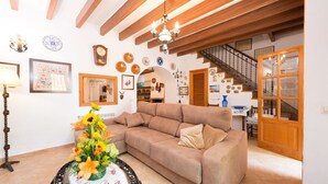 A cozy living room with a brown sofa, a round table with a floral centerpiece, and a staircase leading to another level. - Can Fiolet in Algaida (Algaida)