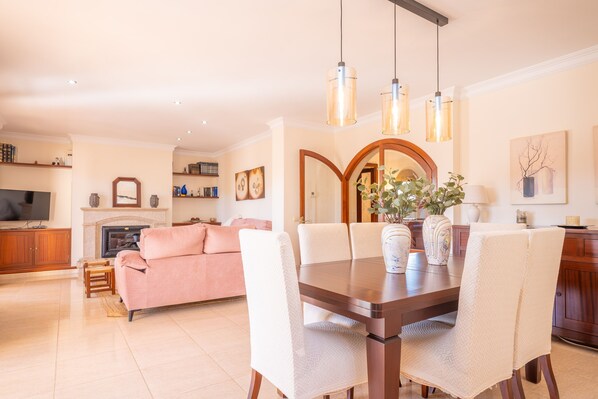 Un salon moderne comprenant une table à manger, des chaises, une cheminée et un téléviseur.