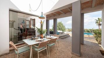 Un patio exterior con una mesa lista para comer, rodeado de sillas y vistas a una piscina y jardines.