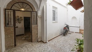 A narrow courtyard with a white wall, a metal gate, a scooter parked, and a potted plant. - Apartamento Arcos Centro (Arcos de la Frontera)
