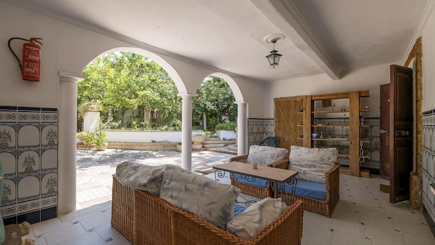 A spacious patio area with wicker furniture, a tiled floor, and a view of greenery through arches.